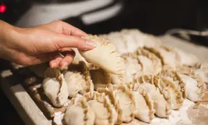 Dłoń trzyma surowe pierogi, gotowe do wrzucenia do gotującej wody.