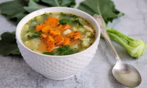 Aksamitna zupa z kalarepy i marchewki, pełna świeżych warzyw i ziół, podana w białej miseczce.