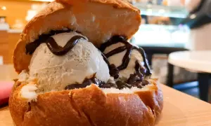 Pyszne lody w brioszce, polane czekoladą, na drewnianej desce.