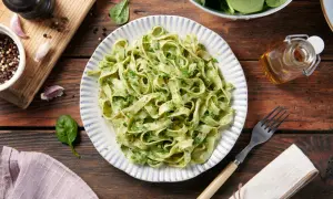 Pyszne dania z makaronem tagliatelle z zielonym pesto, podane na talerzu z niebieskimi paskami. Obok świeży szpinak, czosnek i przyprawy.