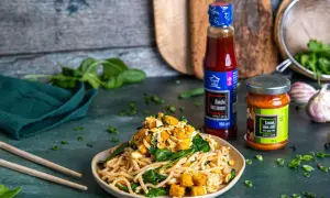 Pyszny makaron po koreańsku z tofu, szpinakiem i sosem kimchi. Obok butelka sosu i słoiczek pasty czosnek-imbir-chili.