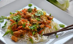 Pyszny makaron z pak choi, kurczakiem i warzywami, posypany sezamem i świeżą kolendrą. Danie prezentuje się apetycznie.