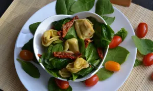 Pyszne tortellini z suszonymi pomidorami i świeżym szpinakiem, ozdobione pomidorkami koktajlowymi.