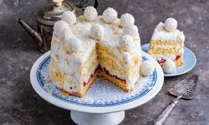 Puszysty tort z kremem rafaello, obsypany wiórkami kokosowymi i migdałami, ozdobiony kulkami Rafaello.