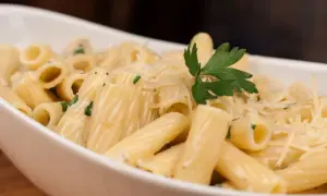 Pyszny makaron z parmezanem, udekorowany natką pietruszki, w białej misce.