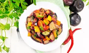 Kolorowa sałatka ze śliwkami, papryką i bakłażanem, ozdobiona natką pietruszki. Obok leżą świeże śliwki i papryczki chili.