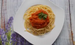 Spaghetti ze świeżych pomidorów, udekorowane natką pietruszki, na białym talerzu, na tle drewnianego blatu i lawendy.