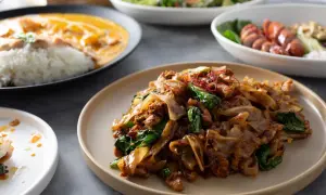 Pyszny pad thai makaron z kurczakiem i warzywami, podany na talerzu. Obok widać inne dania.