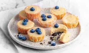 Pyszne serniczki Oreo z jagodami na talerzu. Jeden serniczek jest przekrojony, ukazując kremowe wnętrze i ciemny spód.