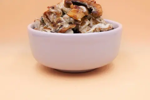 Tofu z pieczarkami w kremowym sosie, podane w białej miseczce.