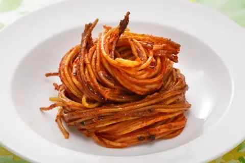 Spaghetti all'assassina, lekko przypieczone, w intensywnym sosie pomidorowym, ułożone na białym talerzu.