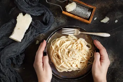 Idealny ser do spaghetti? Ten parmezan starty na tarce i kawałek obok talerza z makaronem sugerują odpowiedź.