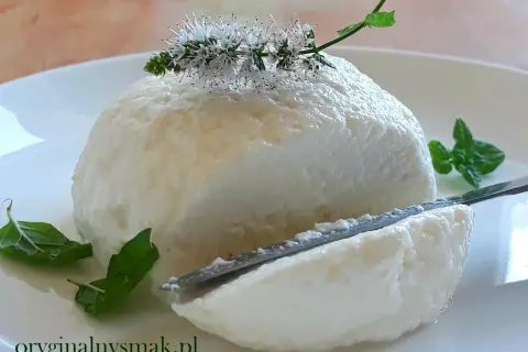 Puszysta, domowa ricotta na talerzu, ozdobiona kwiatami mięty. Nóż delikatnie kroi ser, odsłaniając jego kremową konsystencję.