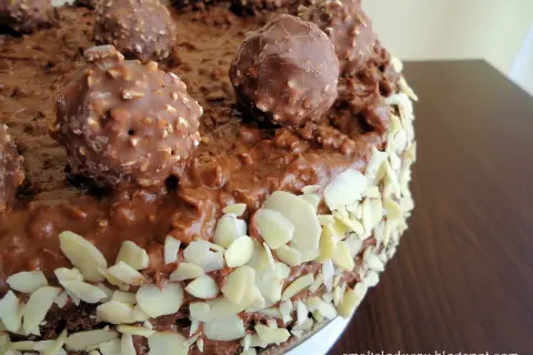 Pyszny tort Ferrero Rocher, obficie udekorowany czekoladowymi kulkami i płatkami migdałów.