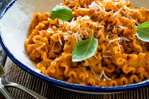 Pyszna włoska pasta z sosem pomidorowym, posypana parmezanem i udekorowana listkami bazylii. Idealna na obiad.