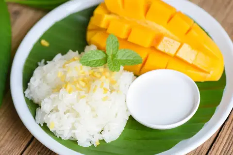Pyszny mango sticky rice: soczyste mango, kleisty ryż, mleczko kokosowe i listek mięty na liściu bananowca.