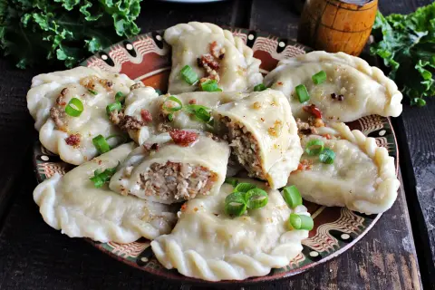 Pyszne pierogi z kaszą gryczaną i serem białym, okraszone skwarkami i szczypiorkiem, na ozdobnym talerzu.