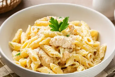 Pyszne danie z makaronem penne w kremowym sosie z kurczakiem, udekorowane natką pietruszki.