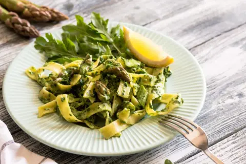 Pyszny makaron ze szparagami i zielonym pesto, udekorowany cytryną i rukolą. Idealne danie na wiosnę.