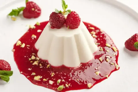 Panna cotta przepis: aksamitny deser z malinowym sosem, pistacjami i świeżymi malinami. Idealny na letnie popołudnie.