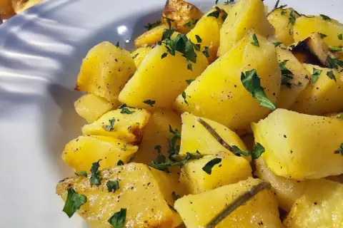 Pieczone ziemniaki pokrojone w ćwiartki, posypane natką pietruszki i pieprzem, podane na białym talerzu.