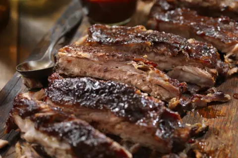 Soczyste żeberka w piwie, polane gęstym sosem BBQ, prezentują się apetycznie na drewnianej desce.