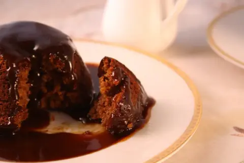 Pyszny, wilgotny deser sticky toffee, polany gęstym, karmelowym sosem, na eleganckim talerzyku.