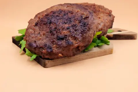 Dwa soczyste kotlety na desce, idealne do burgera. Dowiedz się, jak smażyć burgera, by były tak pyszne!