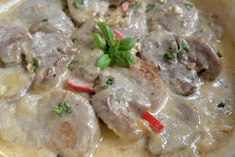 Soczyste polędwiczki w kremowym sosie camembert, udekorowane listkami bazylii i kawałkami papryki. Pyszne danie gotowe do podania.