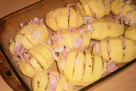 Ziemniaki hasselback z boczkiem i serem, gotowe do pieczenia w naczyniu żaroodpornym.