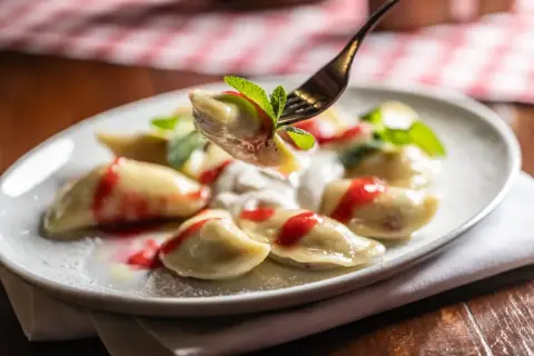 Jak gotować mrożone pierogi? Na talerzu pyszne pierogi z polewą truskawkową i miętą.