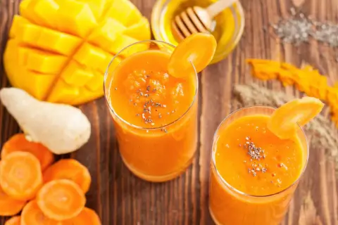 Dwa szklanki pomarańczowego koktajlu z mango i marchewki, ozdobione plasterkiem marchewki i nasionami chia.