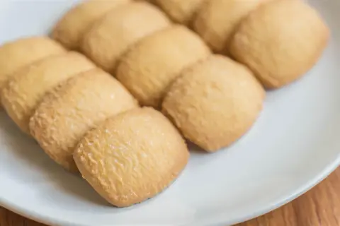 Na białym talerzu ułożone są złociste kocie języczki, posypane cukrem.