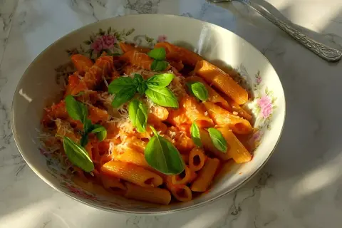 Penne arrabiata z bazylią i parmezanem, podane w ozdobnej misce.
