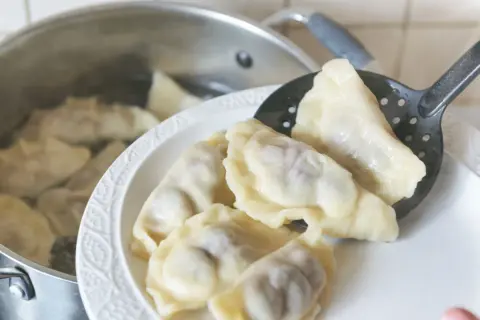 Gorące pierogi wyjmowane łyżką cedzakową z garnka. Czy pierogi przelewa się zimną wodą? Nie, gorące prosto z wody na talerz.