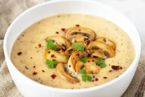 Aksamitny zupa krem z pieczarek, udekorowana plasterkami pieczarek, natką pietruszki i płatkami chili.