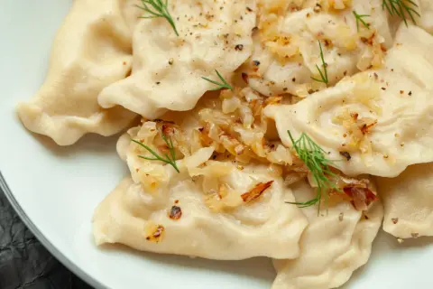 Pyszne pierogi z ziemniakami, okraszone cebulką i koperkiem, posypane pieprzem.