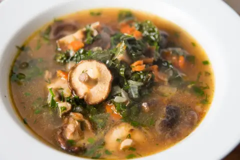 Aromaticzna, tradycyjna zupa grzybowa z kawałkami grzybów shiitake, zielonymi liśćmi i marchewką, podana w białej misce.