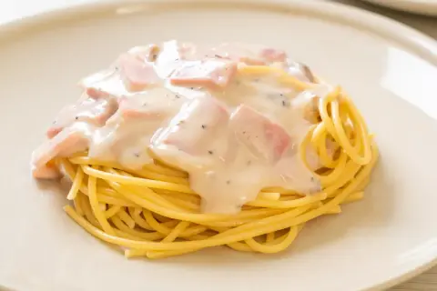 Pyszny makaron z pancettą i kremowym sosem, posypany pieprzem, na jasnym talerzu.