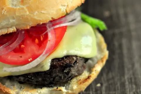 Pyszne burgery z czarnej fasoli z serem, pomidorem i czerwoną cebulą, podane w miękkiej bułce.