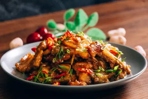 Chrupiąca wieprzowina po chińsku, z papryczkami chili i szczypiorkiem, na szarym talerzu.