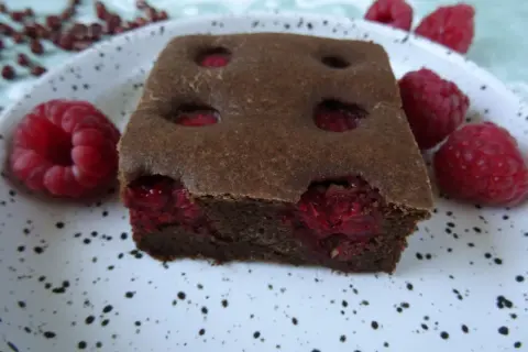 Pyszny fit brownie z fasoli, z malinami w środku i na talerzu. Idealny deser dla łasuchów.