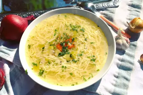 Aromaticzny, złocisty, dobry rosół z makaronem i natką pietruszki, obok cebula i czosnek.
