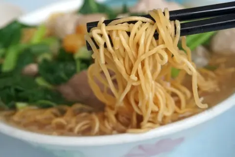 Chopsticks unoszą kłębek złocistego makaronu z miski pełnej aromatycznej domowej zupki chińskiej z warzywami i mięsem.