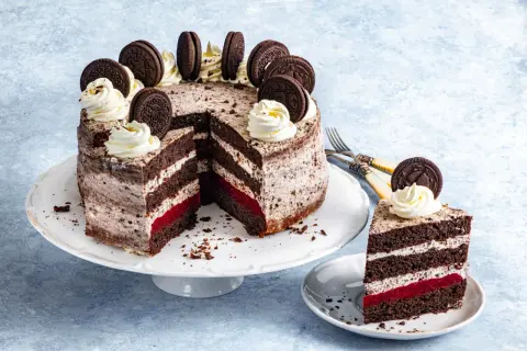 Pyszny tort oreo z kremem, malinową warstwą i ciasteczkami oreo na wierzchu. Kawałek ciasta na talerzyku.