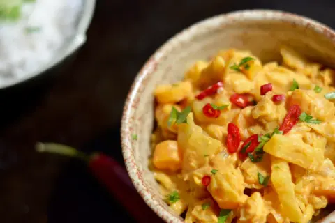 Pyszne danie z ziemniaków i warzyw w kremowym sosie co z mleczka kokosowego, ozdobione papryczką chili i natką pietruszki.