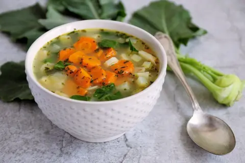 Aksamitna zupa z kalarepy i marchewki, pełna świeżych warzyw i ziół, podana w białej miseczce.