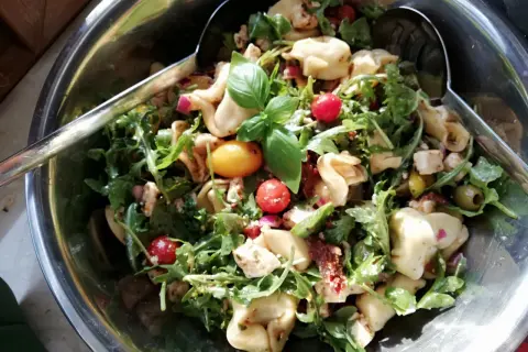 Pyszna sałatka tortellini z rukolą, pomidorkami koktajlowymi, oliwkami i serem feta. Idealna na letnie przyjęcie.
