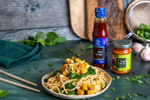 Pyszny makaron po koreańsku z tofu, szpinakiem i sosem kimchi. Obok butelka sosu i słoiczek pasty czosnek-imbir-chili.