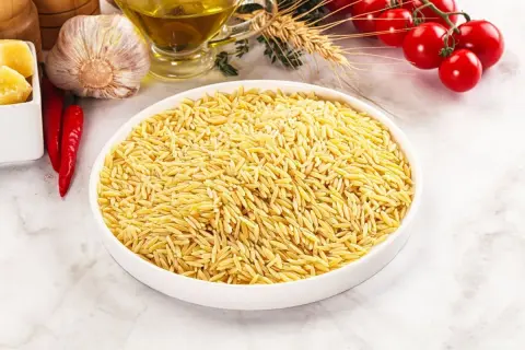 Miseczka pełna drobnego makaronu orzo, obok czosnek, papryczki chili, pomidorki i oliwa.